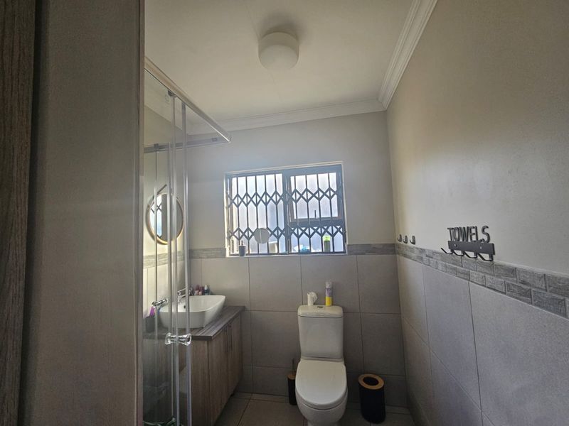 A functional bathroom featuring a vanity with a vessel sink, a toilet, and a glass-enclosed shower with neutral wall tiling.