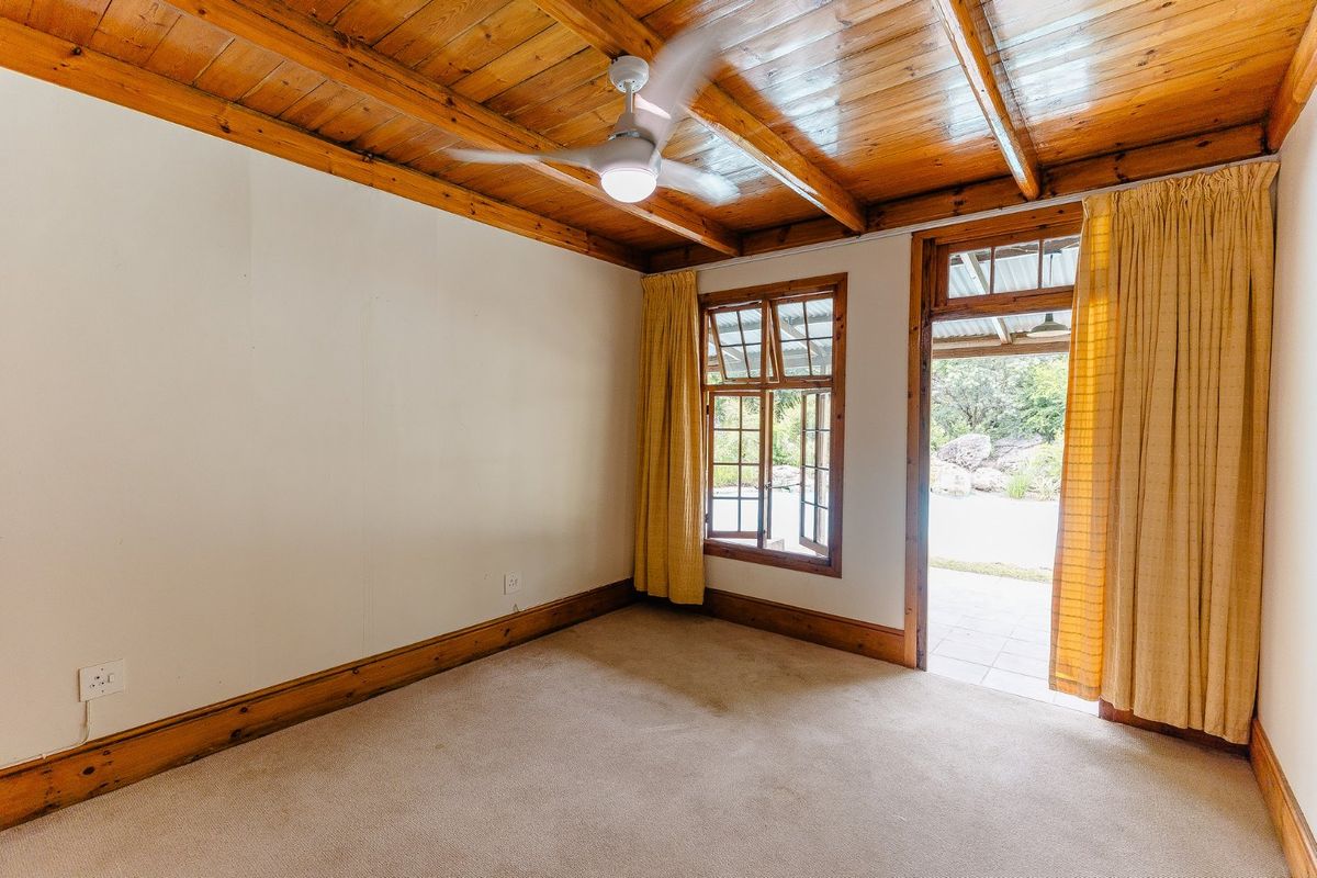 A bright, empty bedroom featuring exposed timber beam ceilings, timber-framed windows, and direct access to an outdoor patio area.