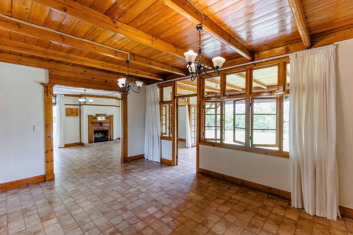 Spacious living area featuring exposed timber beam ceilings, tiled flooring, and a built-in fireplace, offering a warm and rustic atmosphere.
