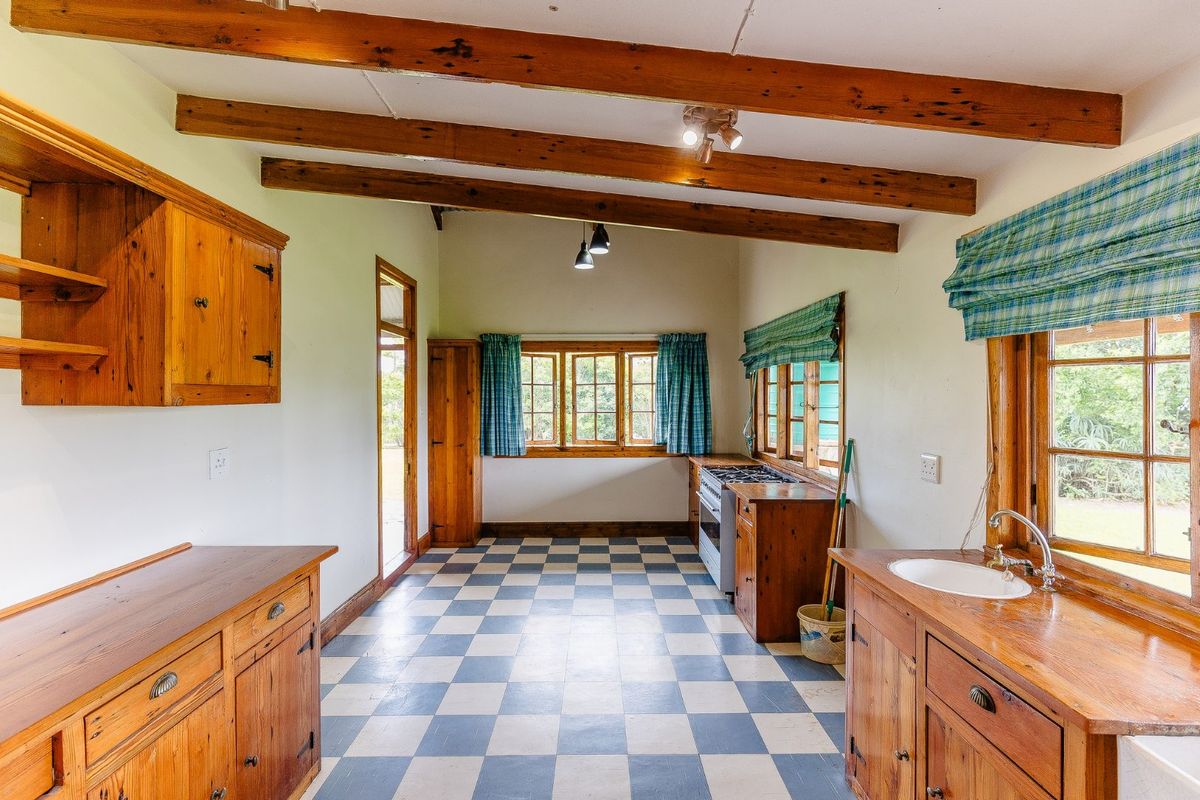 A rustic farmhouse kitchen featuring exposed timber beams, checkered flooring, built-in wooden cabinetry, and a gas stove with ample natural light.