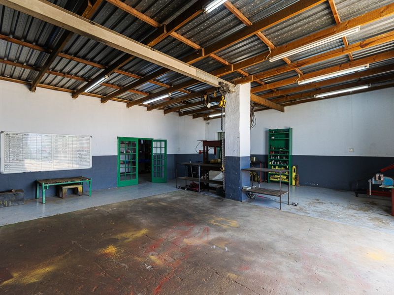 A spacious utility or workshop area featuring exposed timber roof trusses, corrugated metal roofing, concrete flooring, and functional built-in shelving.