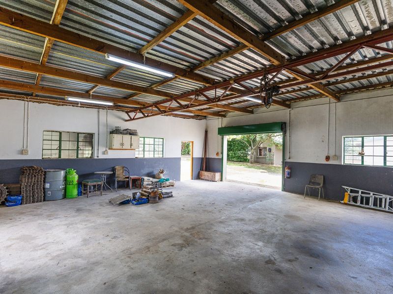 Spacious farm garage or workshop featuring exposed timber roof trusses, concrete flooring, and large access doors, suitable for storage or agricultural equipment maintenance.