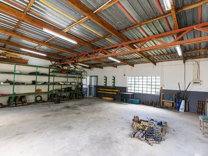 Spacious utility workshop featuring exposed timber roof trusses, concrete flooring, and extensive built-in metal shelving, suitable for farm equipment storage or maintenance.