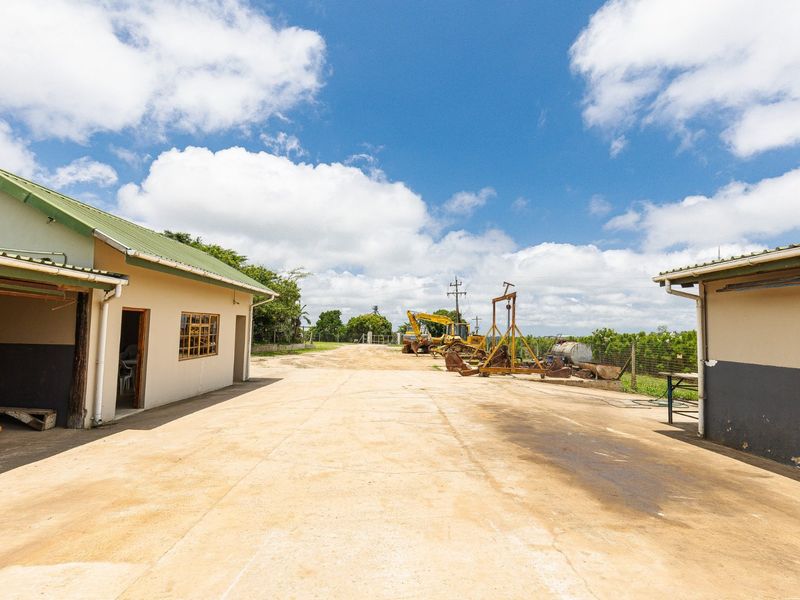 A spacious concrete yard area situated between two farm buildings, featuring metal roofing and open access to the surrounding property grounds.