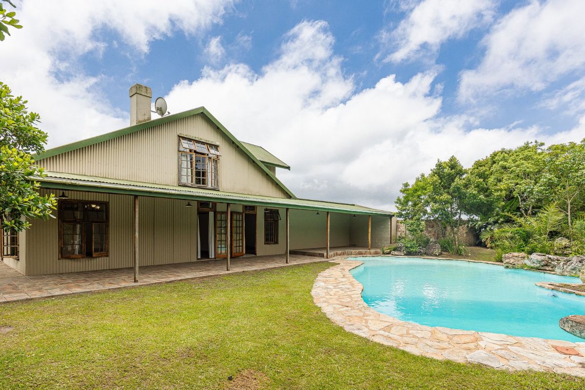 Rear view of a farm-style residence featuring corrugated metal cladding, a spacious covered patio, and a landscaped swimming pool area.
