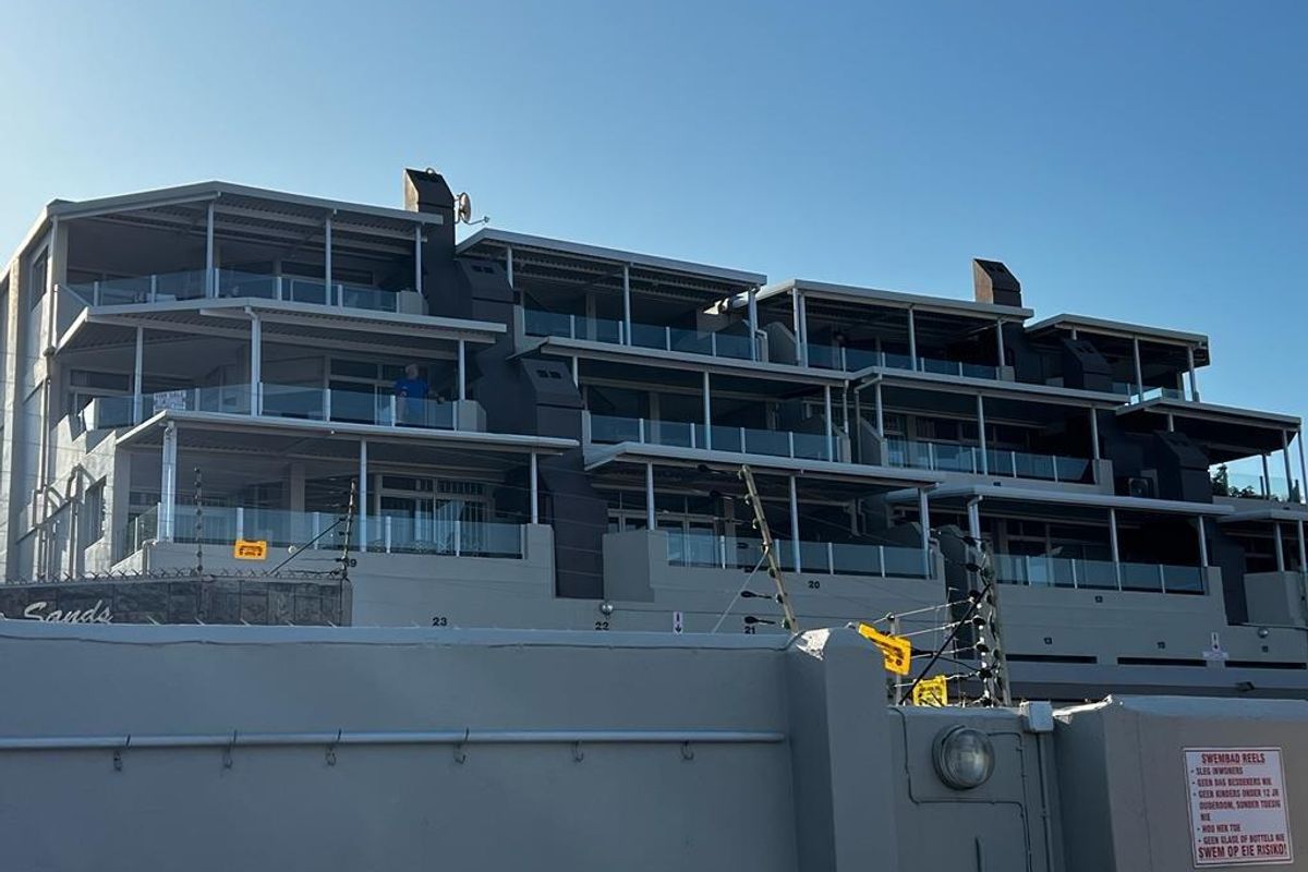 Rear elevation of a multi-story apartment complex featuring private balconies with glass balustrades and secure perimeter walling.