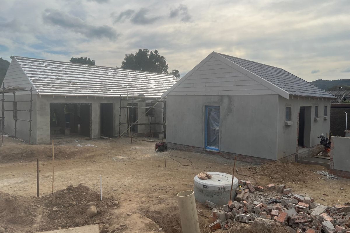 A construction site showing two residential structures in the early stages of development with unfinished exterior walls and roofing.