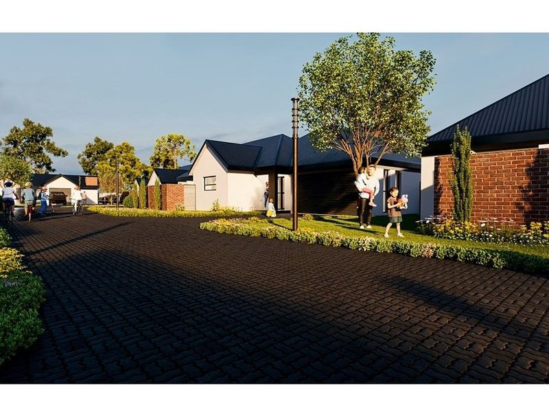 A street-level view of a modern residential development featuring paved driveways, brick and rendered facades, and well-maintained landscaped gardens.