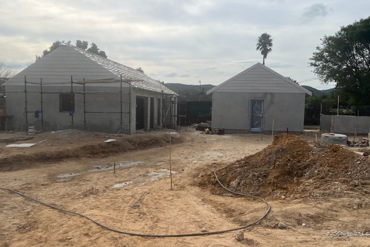 A construction site showing two detached structures in the early stages of development with unfinished exterior walls and scaffolding.