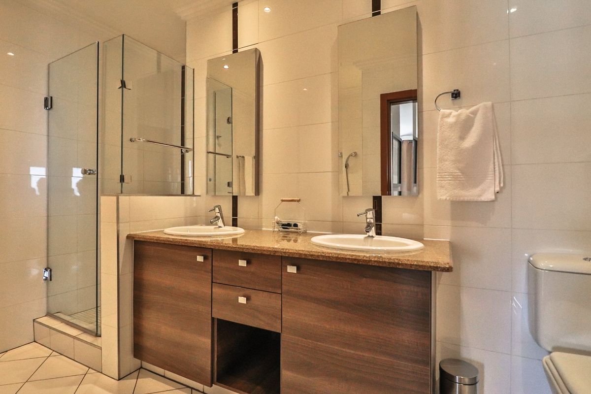 Modern bathroom featuring a double vanity with granite countertop, glass-enclosed shower, and neutral wall tiling.