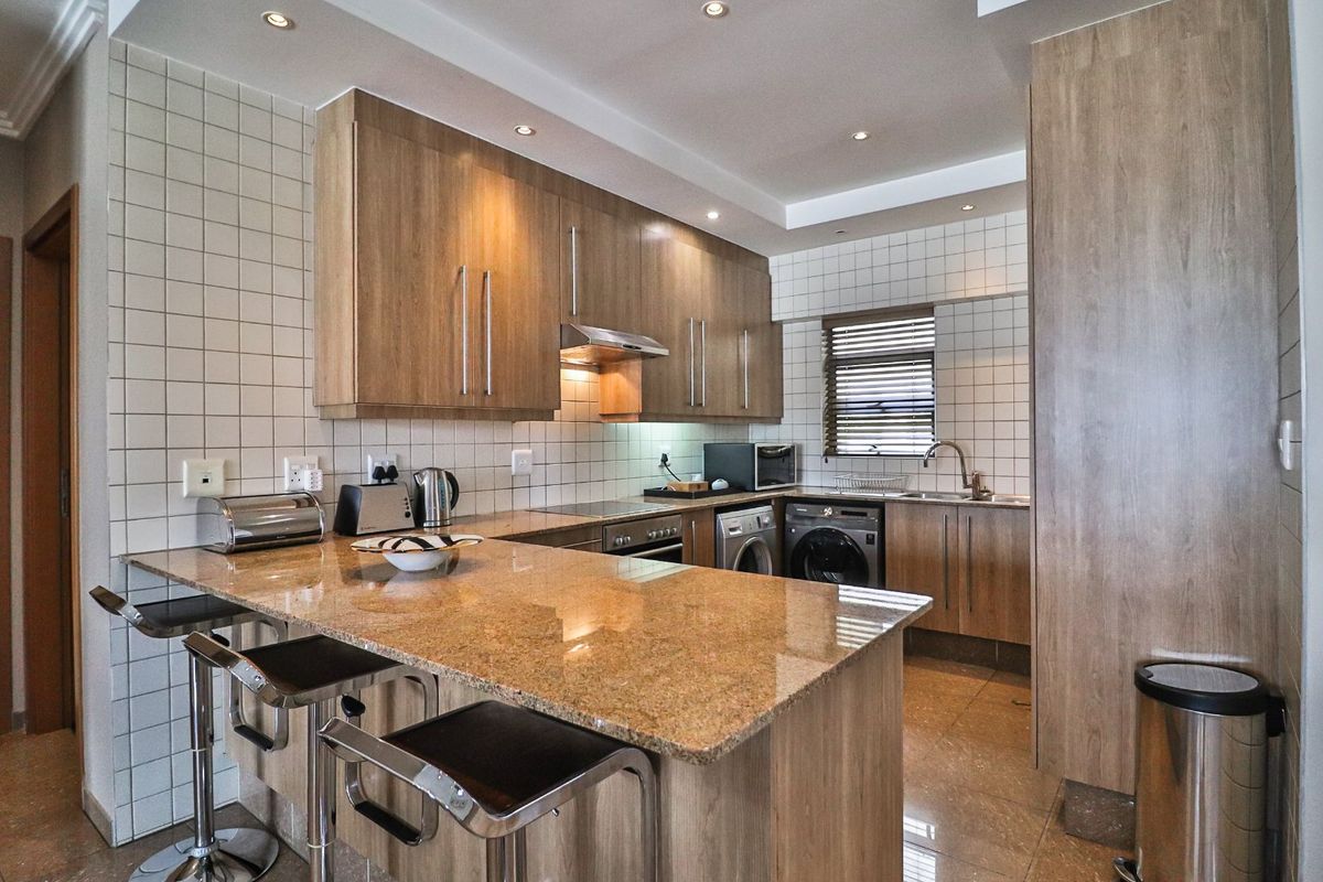 Modern kitchen featuring granite countertops, wood-finish cabinetry, integrated appliances, and a breakfast bar, complemented by recessed lighting and tiled finishes.
