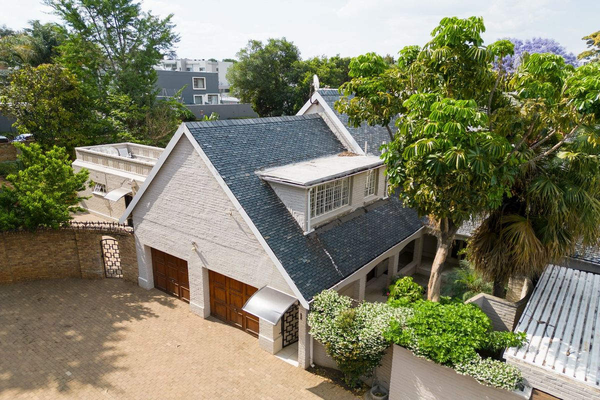 Aerial view of a residential property featuring a slate roof, double garage, and a paved driveway surrounded by mature trees.