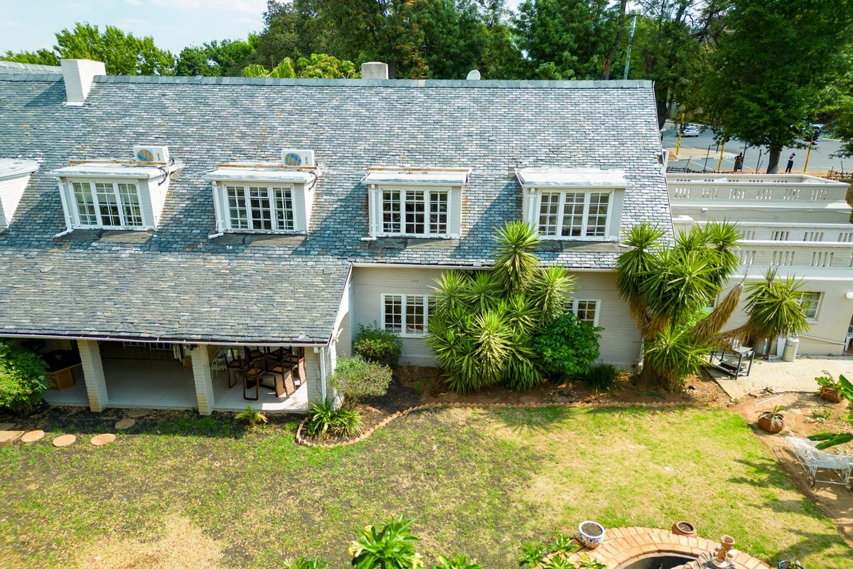 Aerial view of the rear elevation featuring a slate roof with dormer windows, a covered patio area, and a landscaped garden.