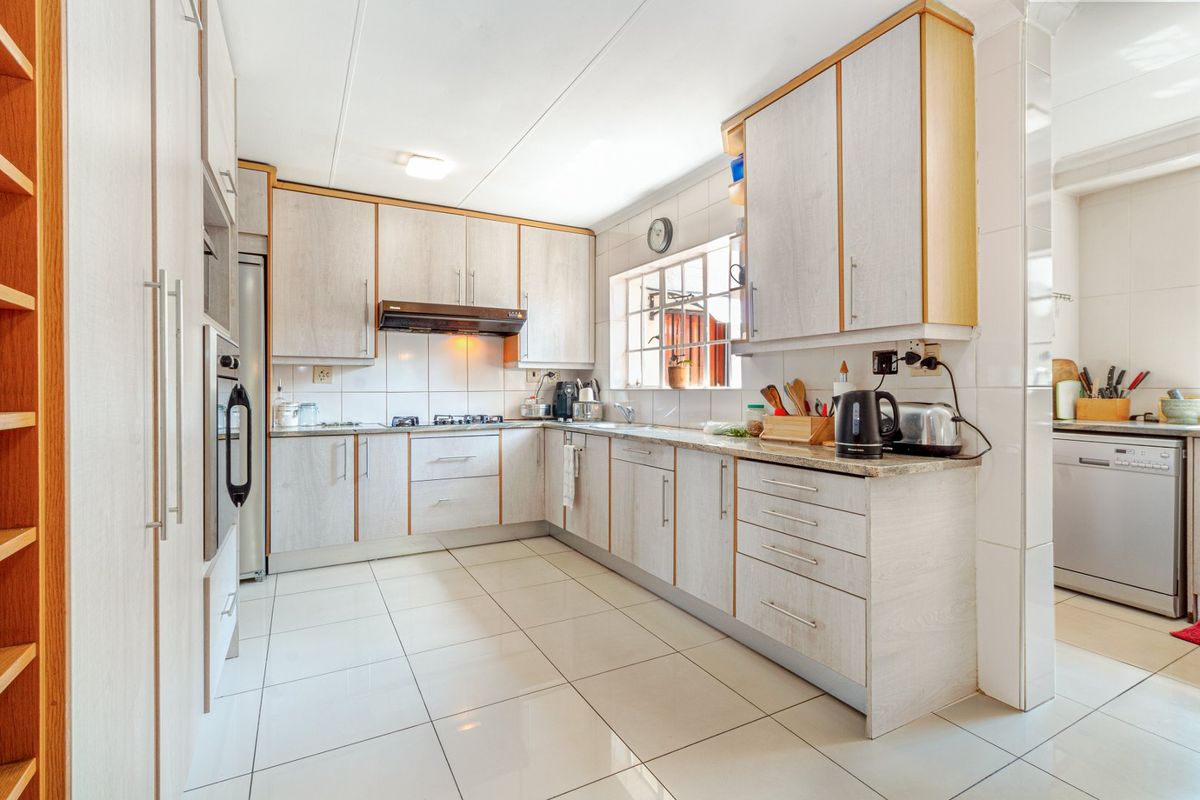 A functional kitchen featuring light wood-grain cabinetry, tiled flooring, a gas hob with extractor fan, and a built-in oven, with an adjacent scullery area.
