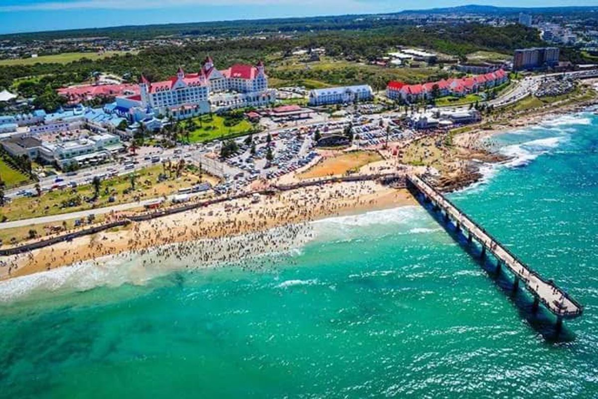An aerial view of the coastal area featuring a prominent pier, sandy beach, and surrounding resort and urban infrastructure.