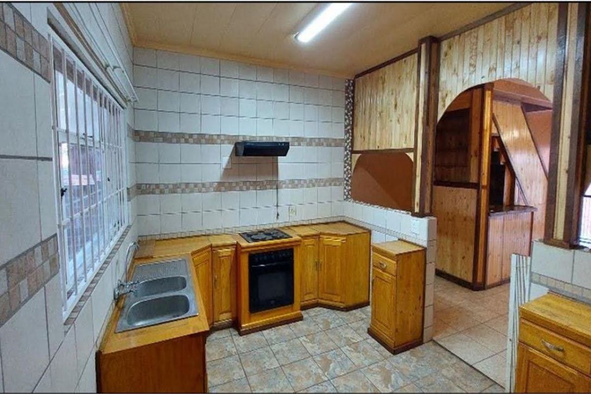 A dated kitchen featuring wooden cabinetry, built-in oven and hob, tiled splashbacks, and tiled flooring, offering a functional layout ready for modernization.