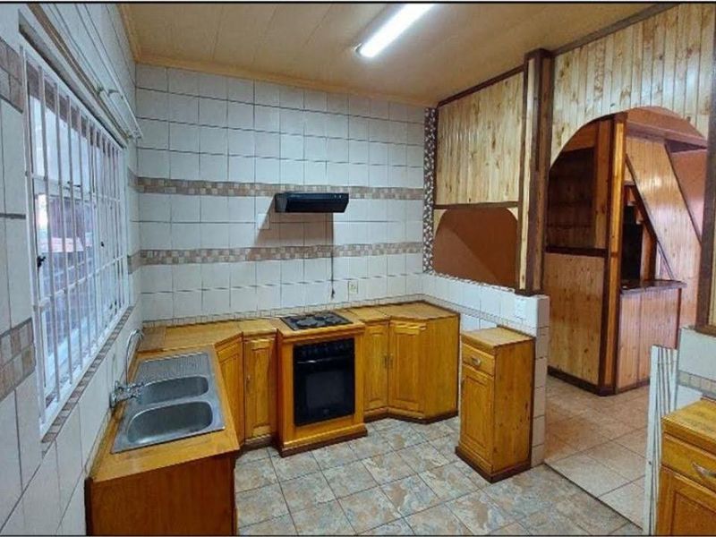A dated kitchen featuring wooden cabinetry, built-in oven and hob, tiled splashbacks, and tiled flooring, offering a functional layout ready for modernization.