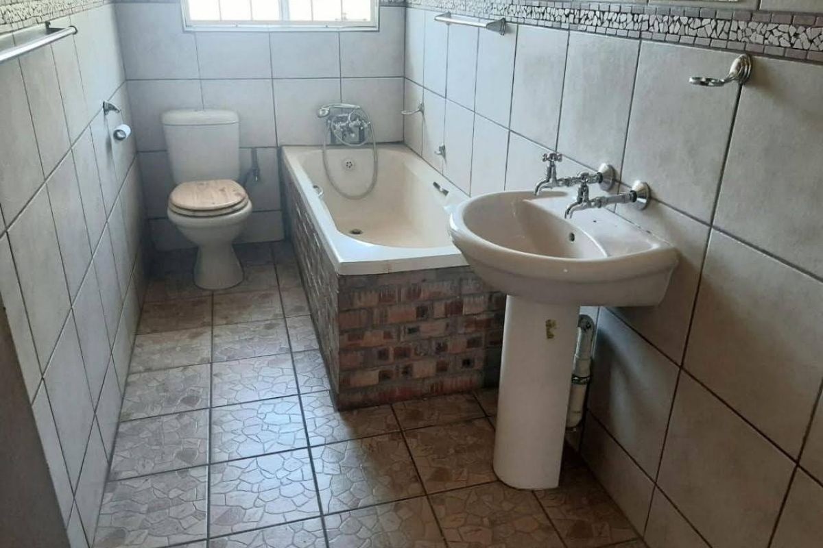 A functional bathroom featuring a pedestal basin, built-in bathtub with brick surround, and full-height wall tiling.