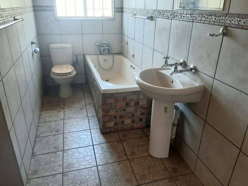 A functional bathroom featuring a pedestal basin, built-in bathtub with brick surround, and full-height wall tiling.
