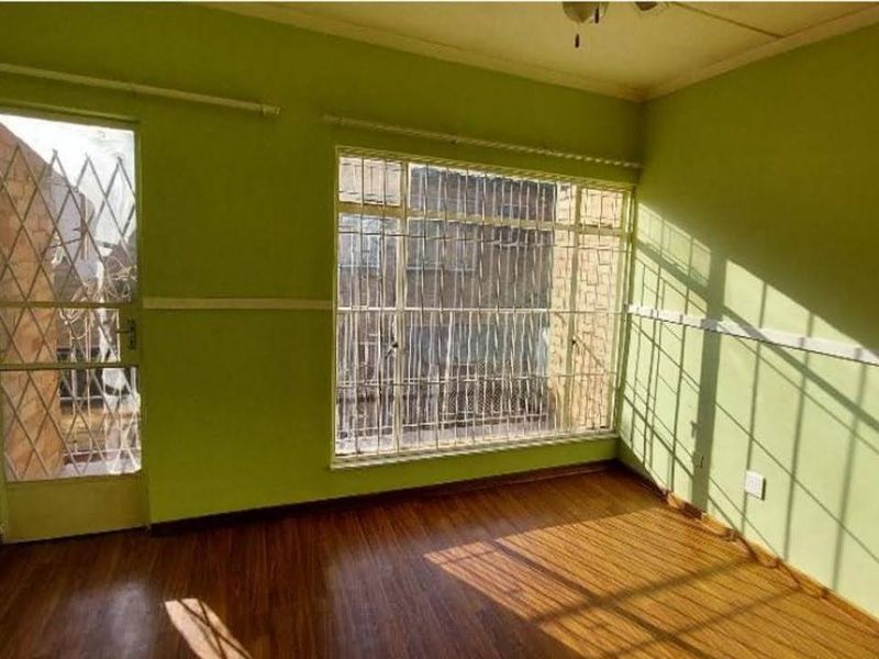 An empty bedroom featuring laminate flooring, security bars on windows and door, and a ceiling fan, ready for a modern update.
