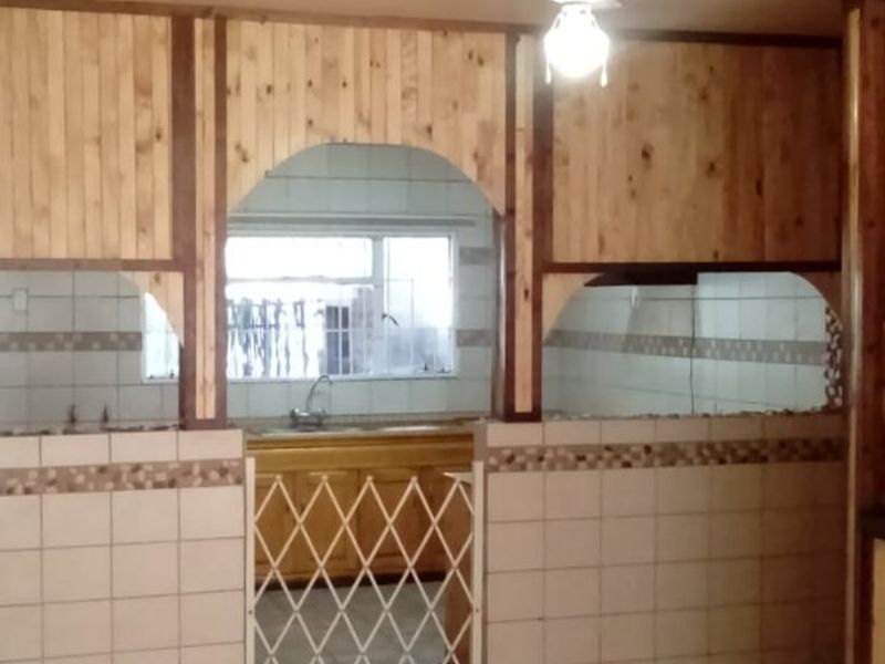 A dated kitchen area featuring wood-paneled walls, tiled flooring, and a built-in sink, currently vacant and ready for renovation.