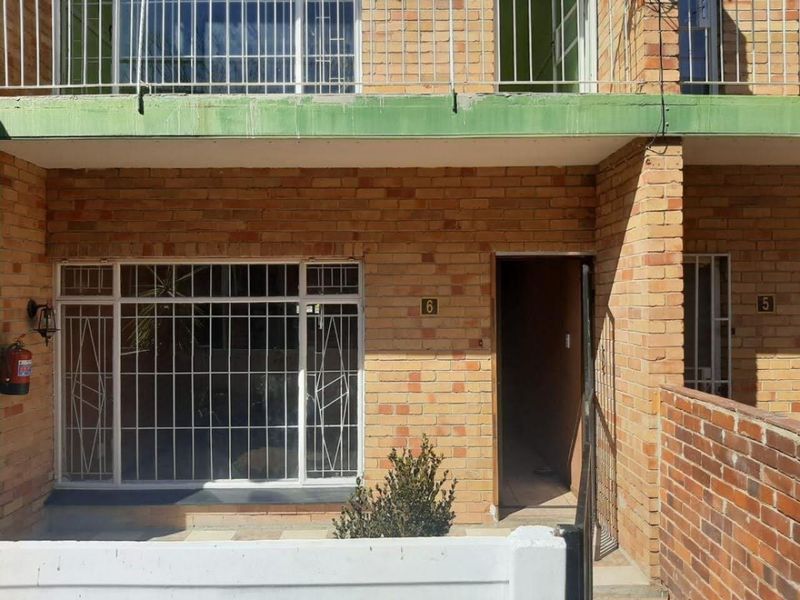 Front elevation of a face brick townhouse featuring a ground floor entrance, security bars on windows, and an upper-level balcony with metal railings.