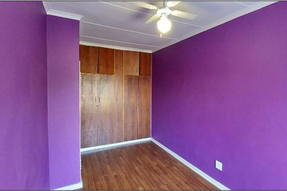 A vacant bedroom featuring laminate flooring, built-in wooden cupboards, and a ceiling fan, finished with vibrant purple wall paint.