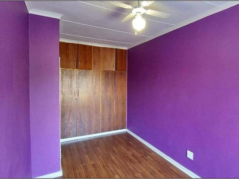 A vacant bedroom featuring laminate flooring, built-in wooden cupboards, and a ceiling fan, finished with vibrant purple wall paint.