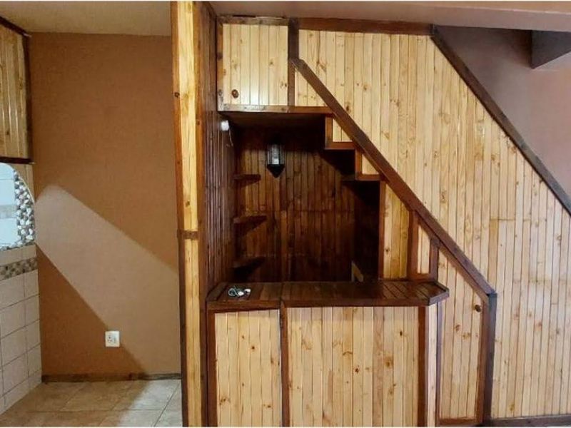 A dedicated bar area featuring custom timber paneling, built-in shelving, and a wooden bar counter, situated beneath a staircase.
