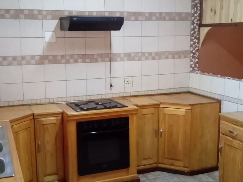 A functional kitchen featuring wooden cabinetry, a built-in oven with hob, extractor fan, and a double bowl sink with tiled backsplash.