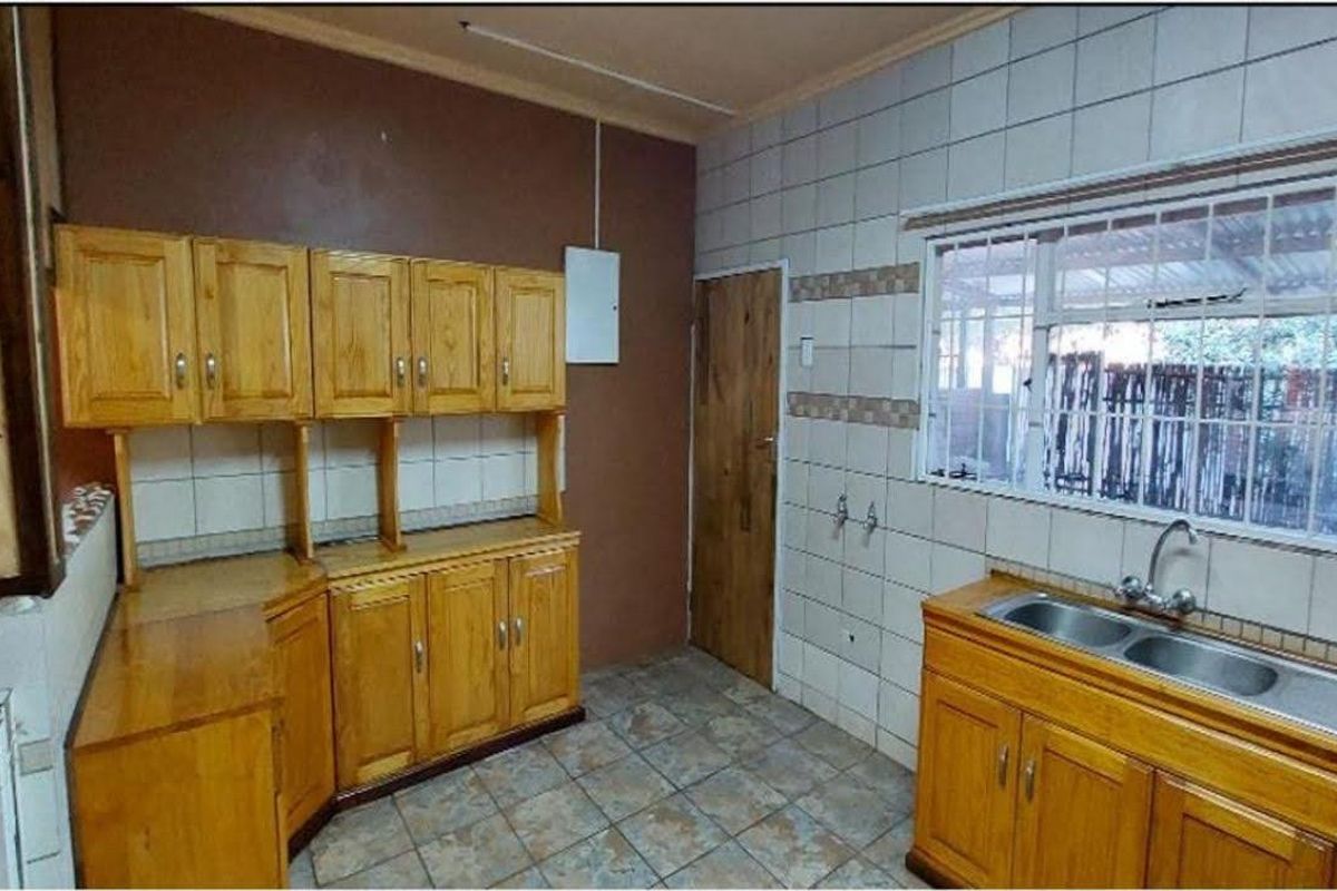 A functional kitchen featuring wooden cabinetry, a double bowl stainless steel sink, tiled splashbacks, and tiled flooring.