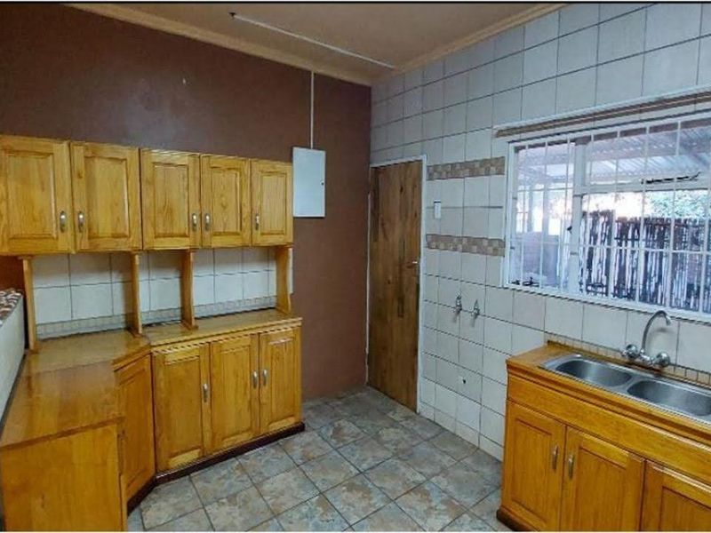 A functional kitchen featuring wooden cabinetry, a double bowl stainless steel sink, tiled splashbacks, and tiled flooring.