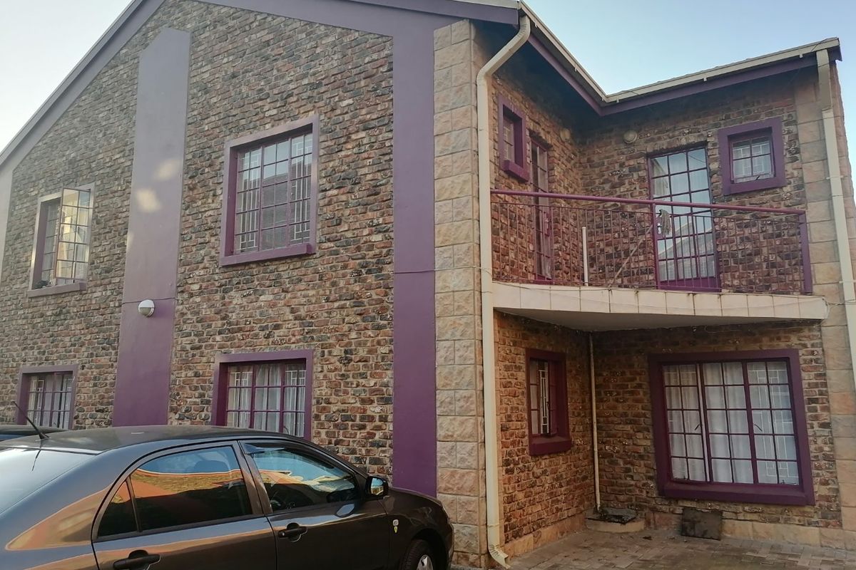 Exterior view of a two-story apartment building featuring a brick facade, a small upper-level balcony with metal railings, and security bars on windows.