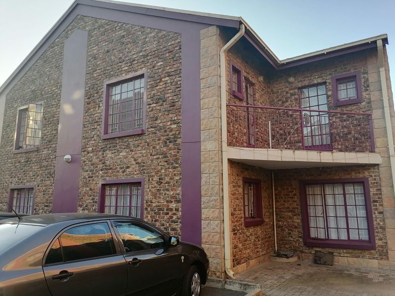 Exterior view of a two-story apartment building featuring a brick facade, a small upper-level balcony with metal railings, and security bars on windows.