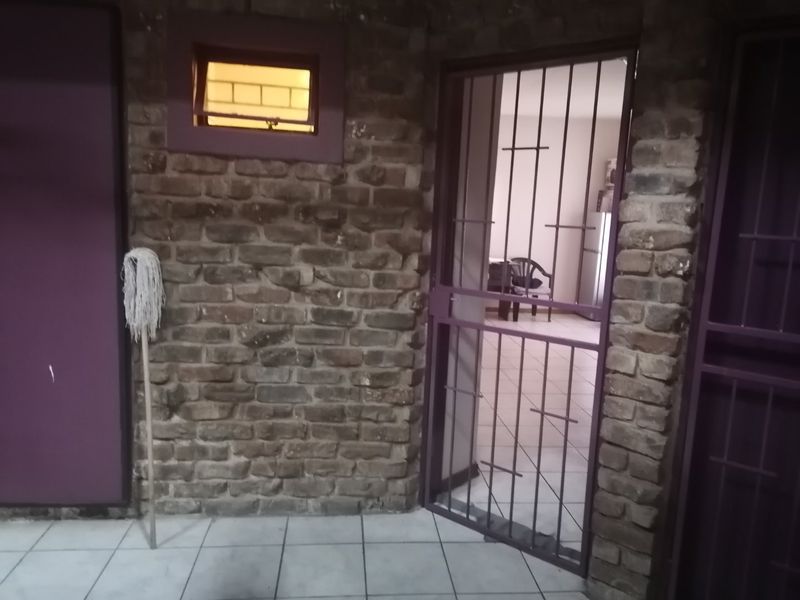 An entry area featuring exposed brick walls, tiled flooring, and a secure metal gate leading into the apartment interior.
