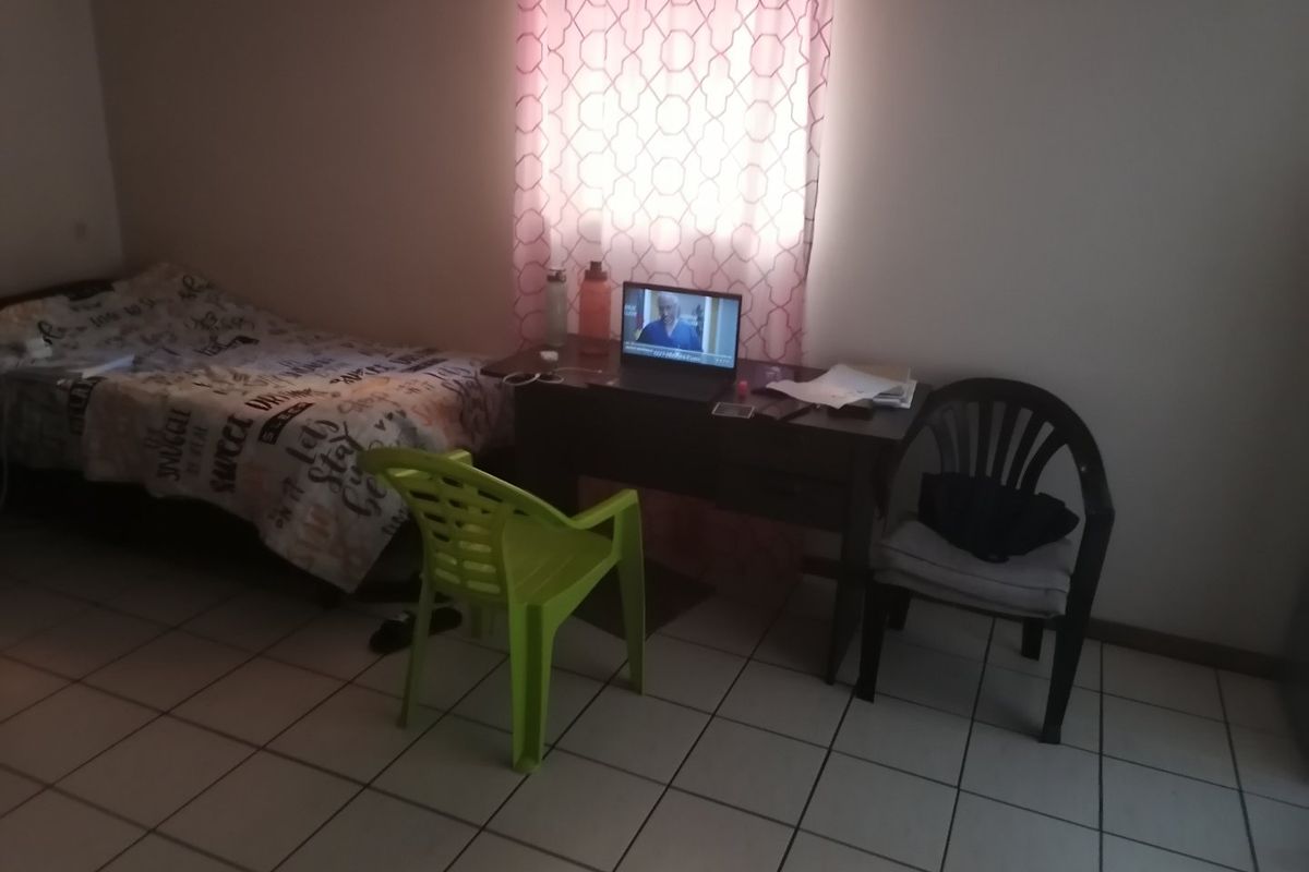 A functional bedroom featuring tiled flooring and a window with curtains, providing a basic living space.