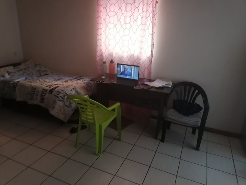 A functional bedroom featuring tiled flooring and a window with curtains, providing a basic living space.