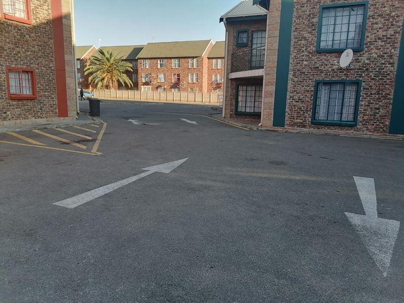 Exterior view of an apartment complex featuring brick facades, paved driveway with directional road markings, and secure window fixtures.