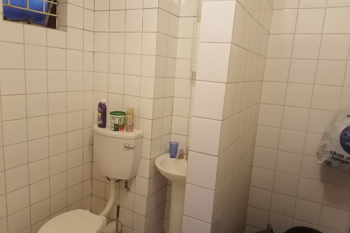 A compact bathroom featuring a pedestal basin and toilet, finished with white ceramic wall tiles throughout.