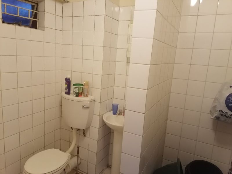 A compact bathroom featuring a pedestal basin and toilet, finished with white ceramic wall tiles throughout.