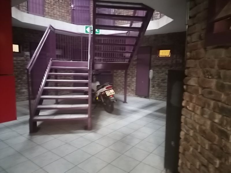 A communal hallway area featuring exposed brick walls, tiled flooring, and a metal staircase leading to upper levels.