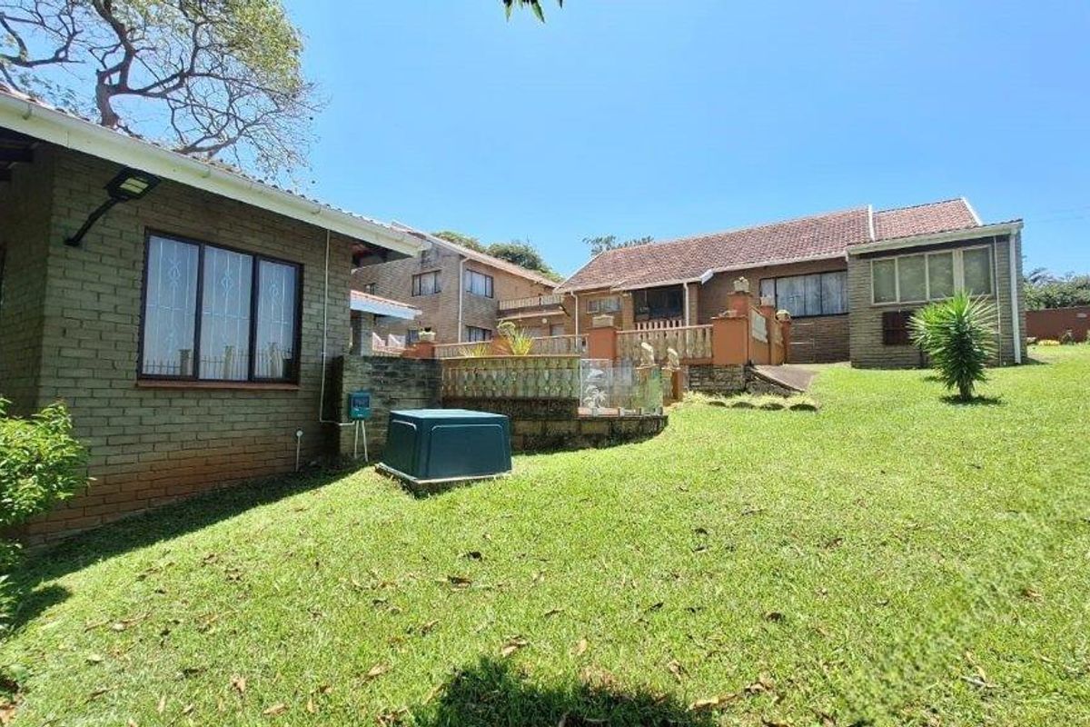 Rear view of the property featuring a brick exterior, tiled roof, and a raised terrace area overlooking the garden.