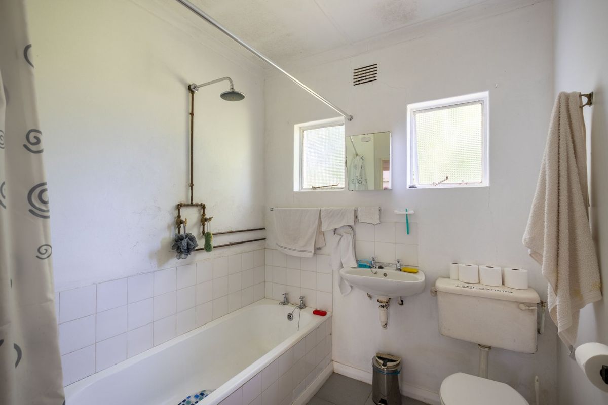 A functional bathroom featuring a bathtub with exposed shower plumbing, a wall-mounted basin, and a toilet, requiring cosmetic updates to modernize the space.