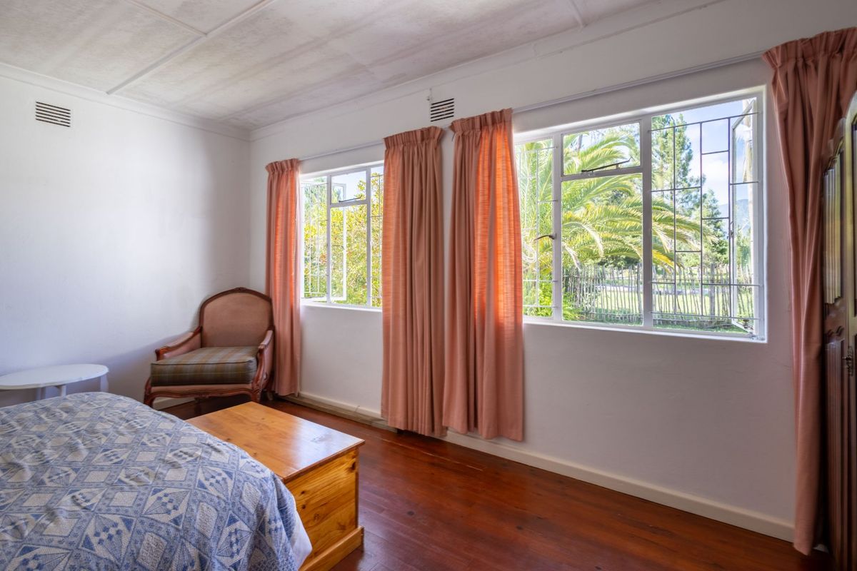 A bedroom featuring original timber flooring, steel-framed windows with security bars, and natural light, offering a classic farm-style aesthetic.