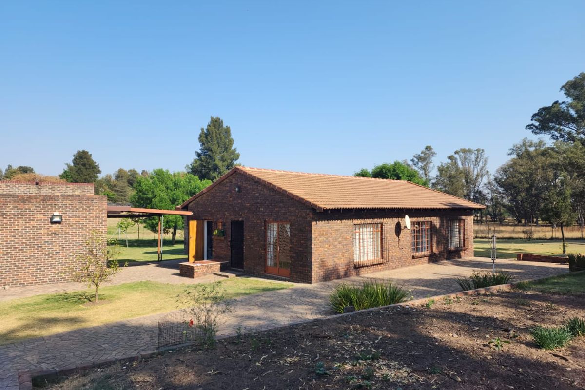 A rear view of a face brick farm house featuring a tiled roof, paved patio area, and established garden surroundings.