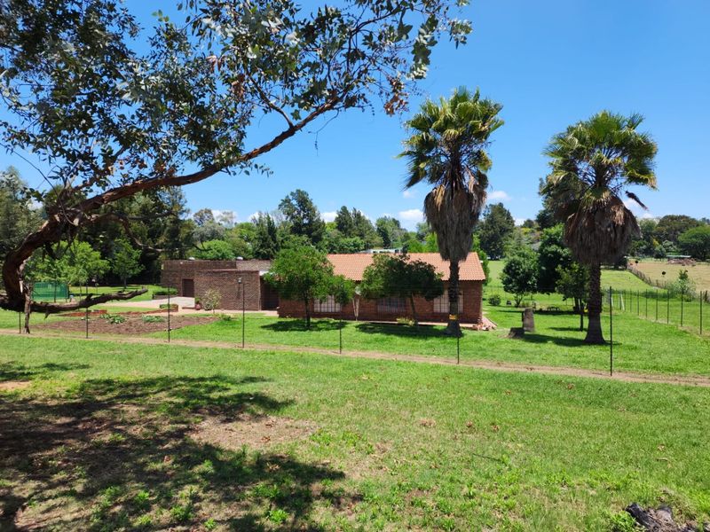 A view of the rear brick farmhouse exterior, featuring a terracotta tiled roof, security window bars, and expansive surrounding garden grounds.