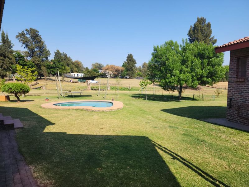 Spacious farm garden featuring a small swimming pool, established trees, and brick exterior wall, offering a peaceful outdoor setting.