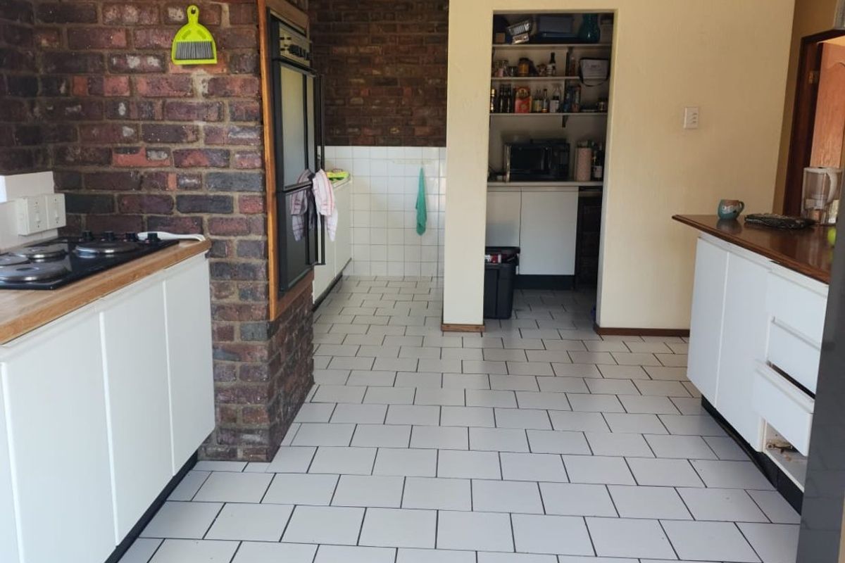 Kitchen featuring white cabinetry, a gas hob, built-in oven, and an exposed brick wall, with an adjacent scullery area and tiled flooring.