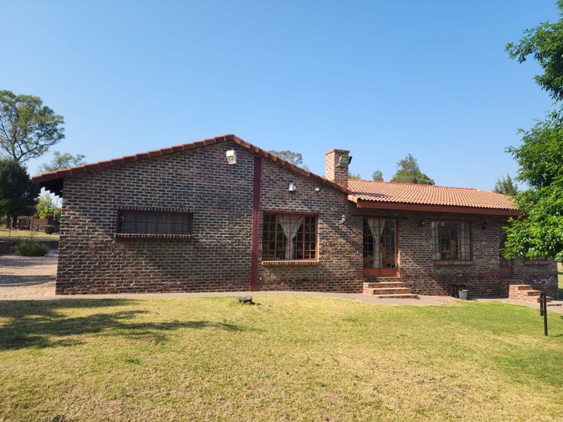 A well-maintained face-brick farmhouse exterior featuring a tiled roof, brick chimney, and secure window fittings, set against a neat lawn.
