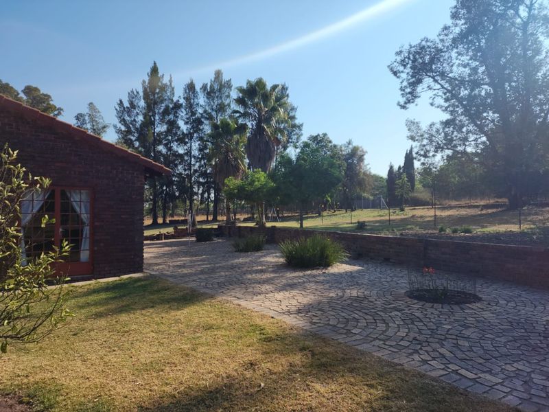 Rear exterior view of a brick farmhouse featuring a cobblestone patio, retaining wall, and established garden landscape.